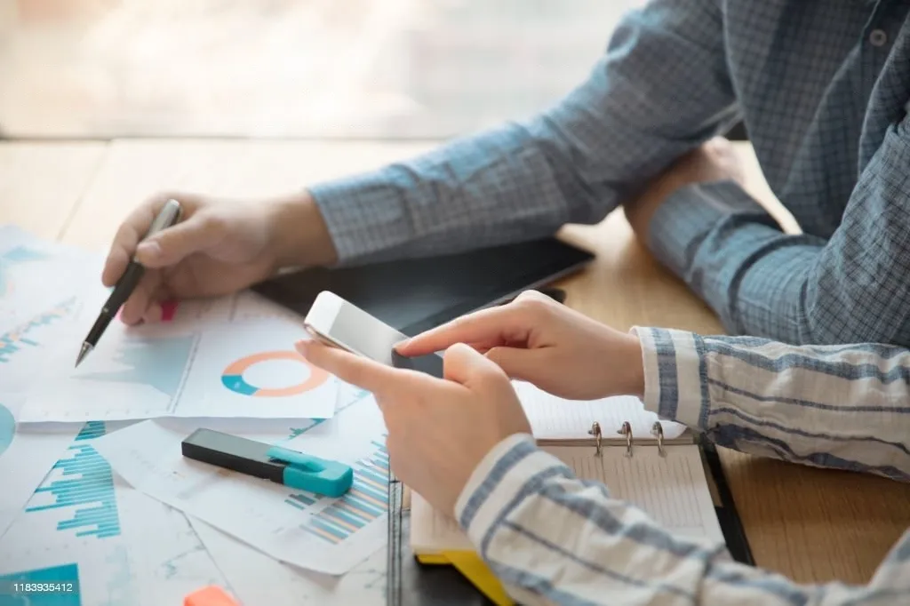 Two people sitting at a table, focused on their cell phones while engaged in conversation discussing about pricing maturity model assessment