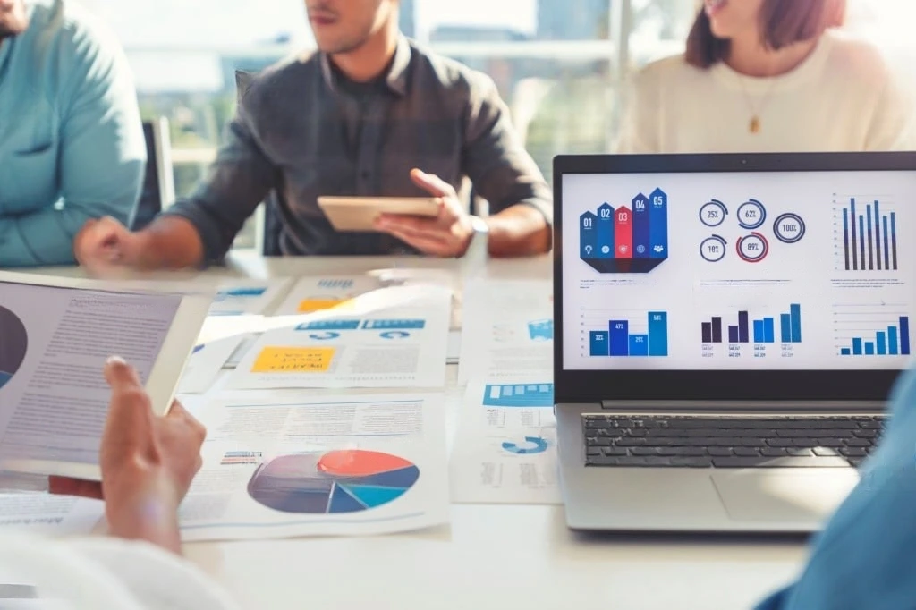 Business professionals collaborating on a laptop displaying various graphs and data analysis about b2b digital transformation meaning