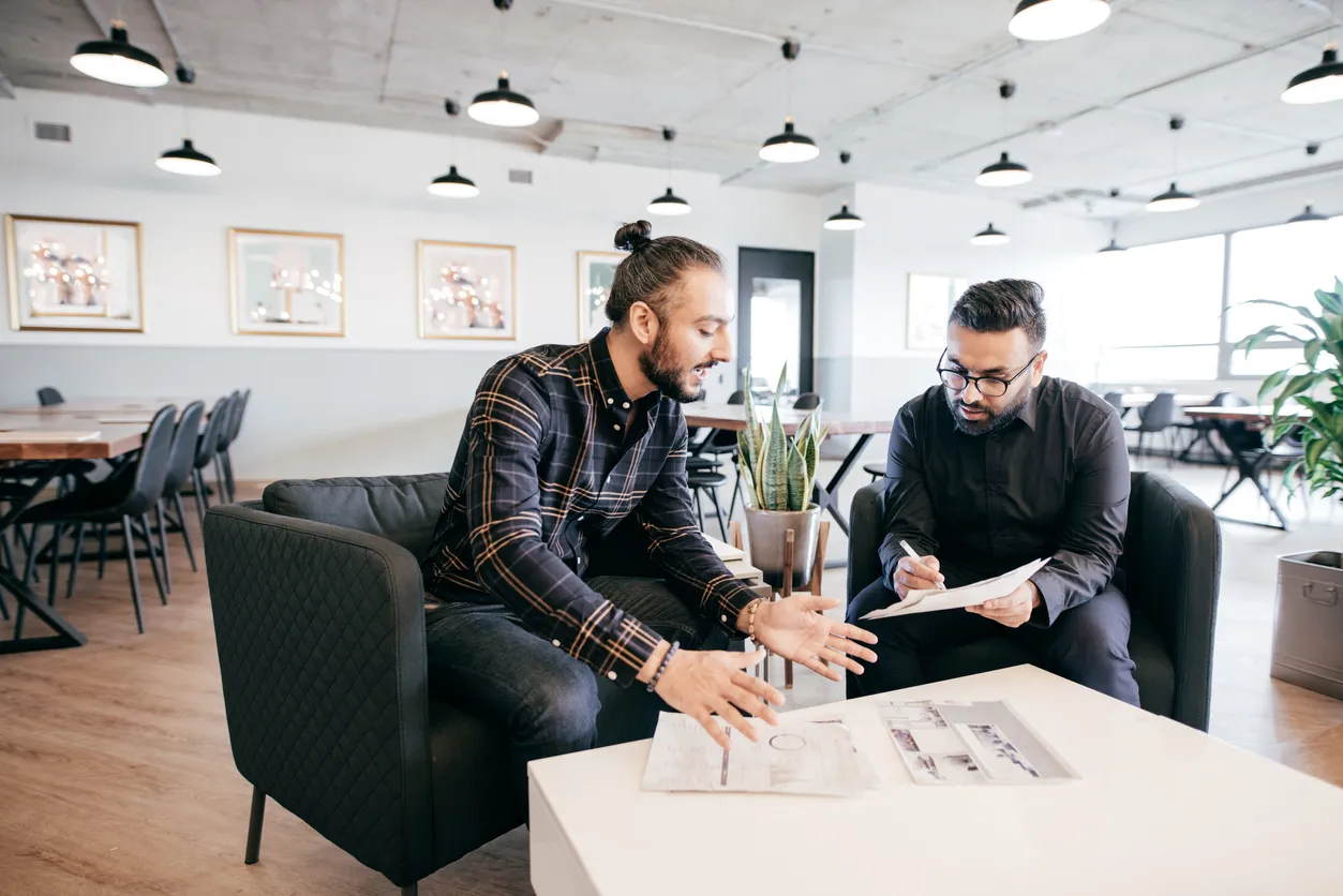 Two men sitting on a couch in an office, engaged in conversation with a relaxed atmosphere discussing what is product marketing in b2b