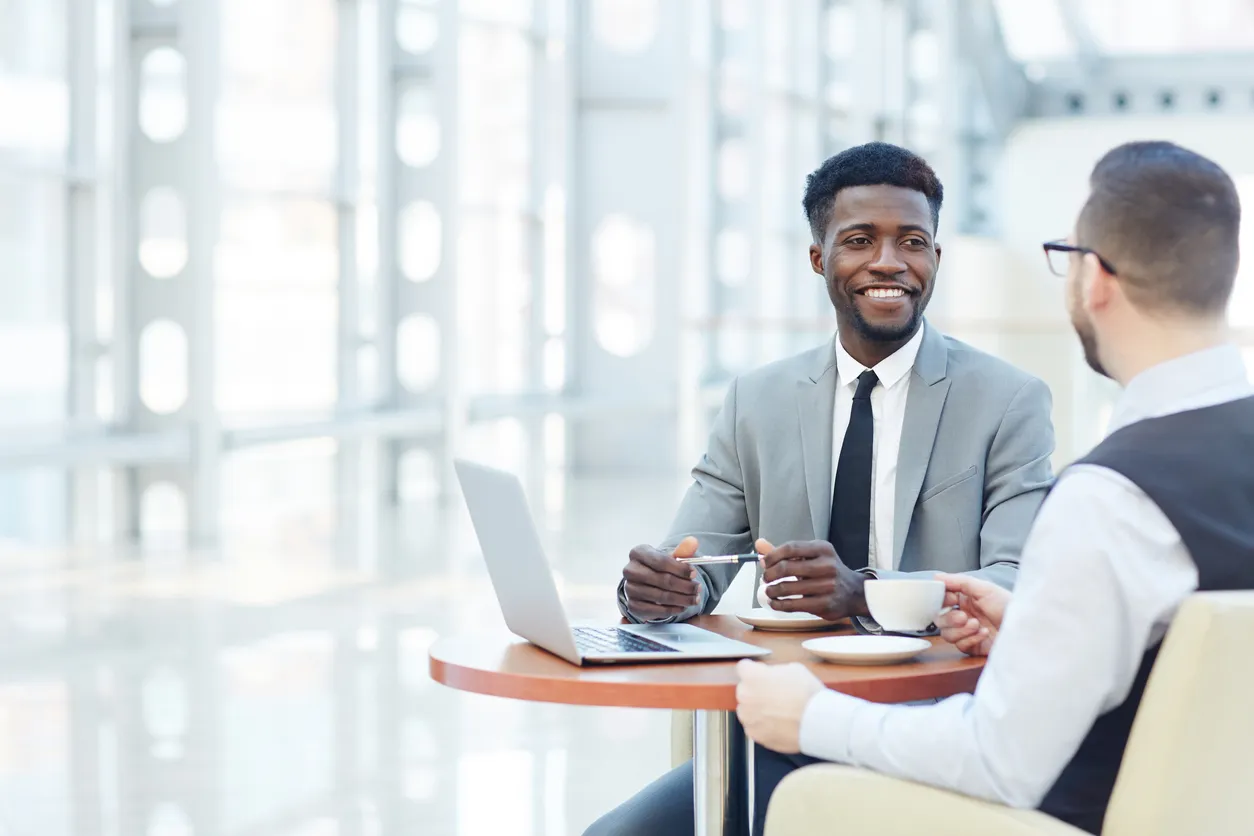 Two men in business suits seated at a table, working together on a laptop discussing b2b buyer journey questions