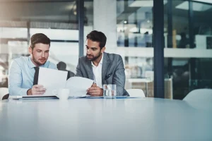 Two business men seated at a table, reviewing documents and discussing details on how to combat commoditization in b2b