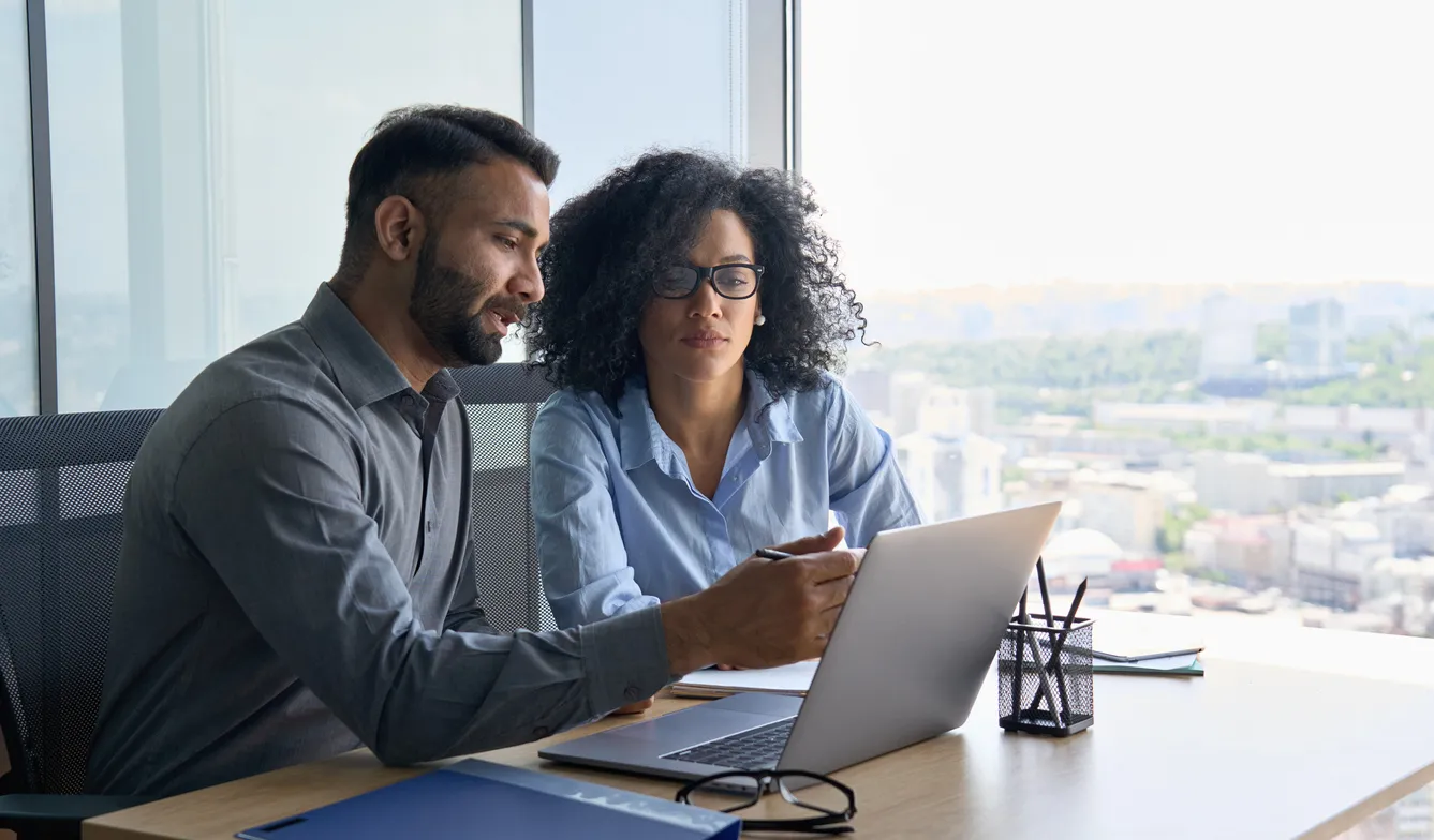 A man and woman seated at a desk, focused on a laptop, engaged in a discussion or collaboration about b2b marketing insights