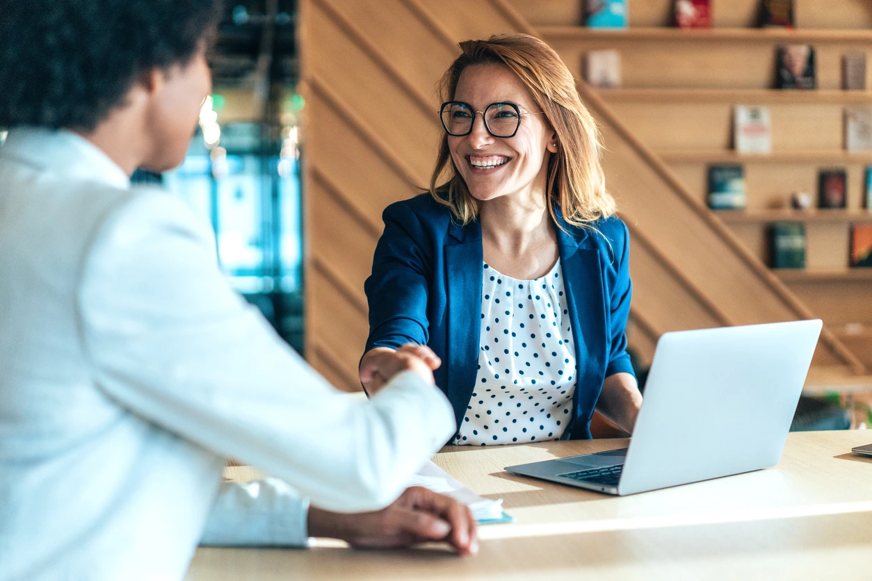 A woman and another woman shake hands at a desk, symbolizing a professional agreement or greeting for go to market strategy saas b2b
