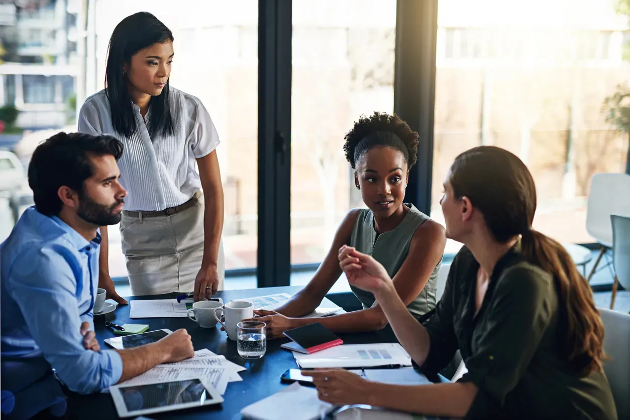 A diverse group of professionals engaged in a discussion during an office meeting around a conference table for marketing performance management