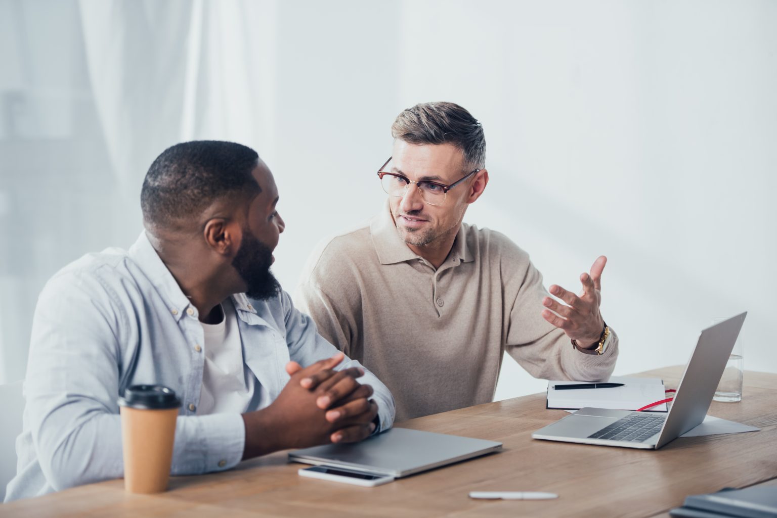 two businessmen sitting at table in office with computers discussing data driven decision making
