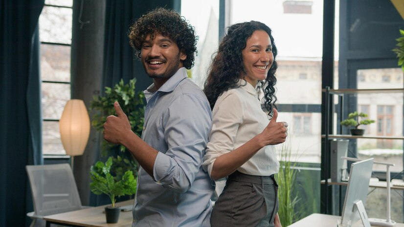 smiling coworkers back to back share a thumbs up in office