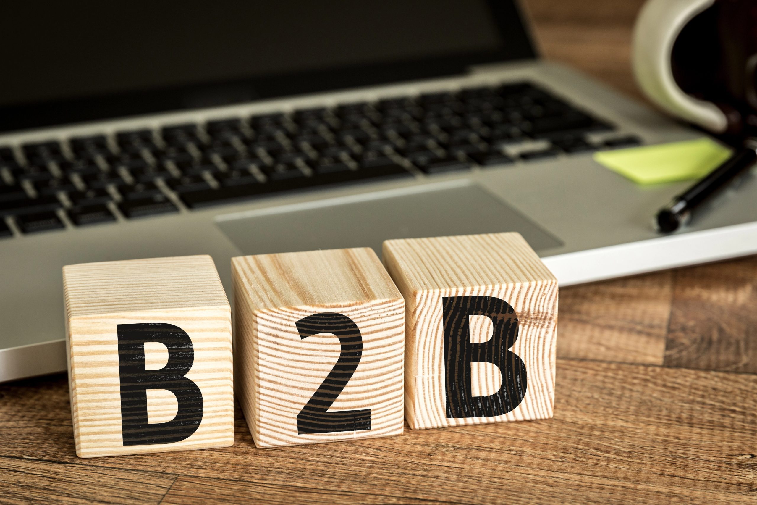 three wooden blocks spelling B2B on work desk with PC in background