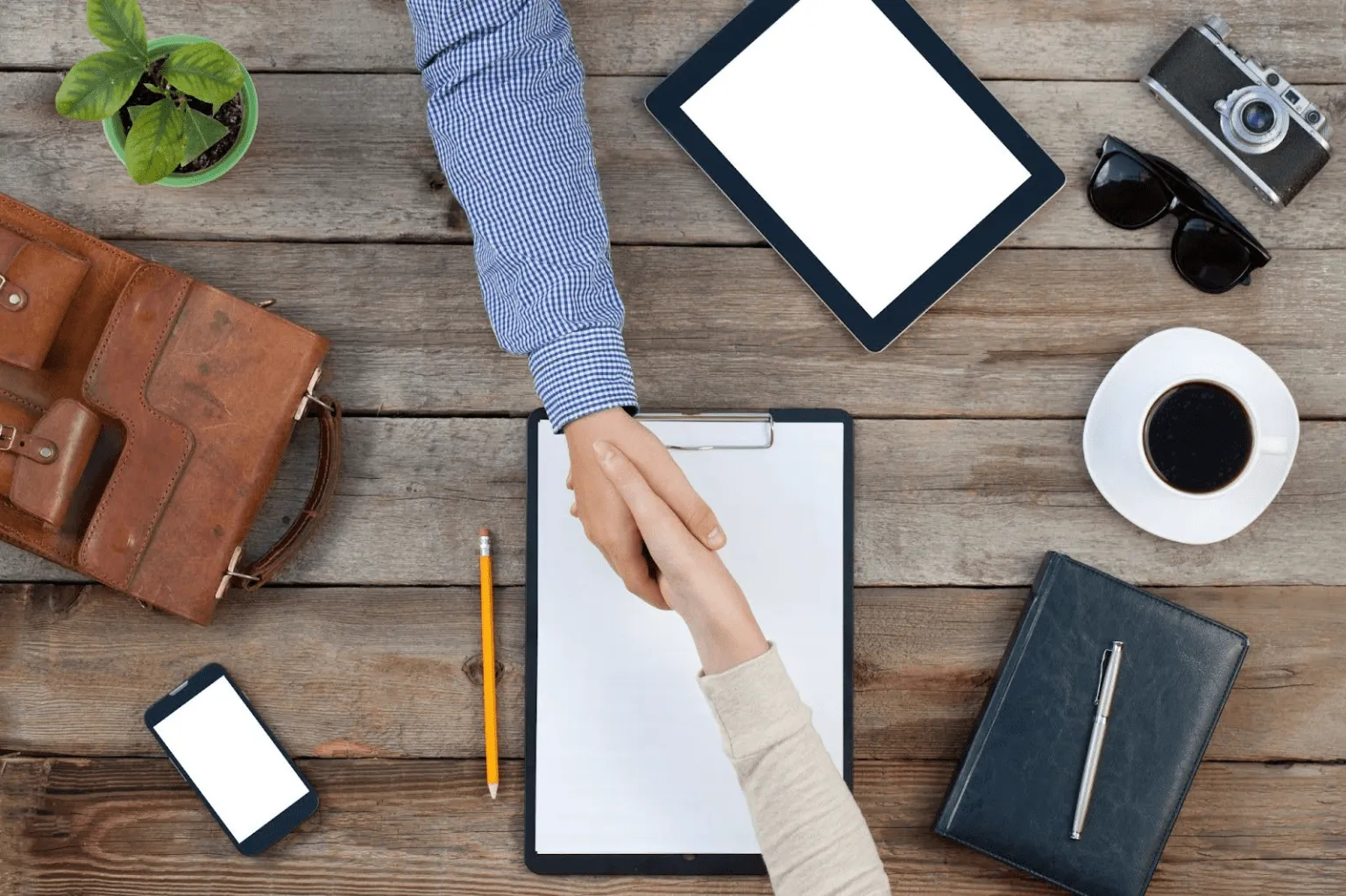 B2B customer engagement concept shown by a handshake across a desk surrounded by business tools and devices.