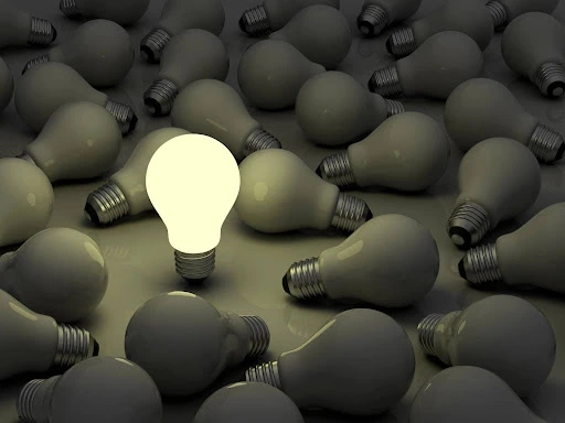 Engineering marketing strategy concept shown by a single glowing light bulb standing out among many unlit bulbs.