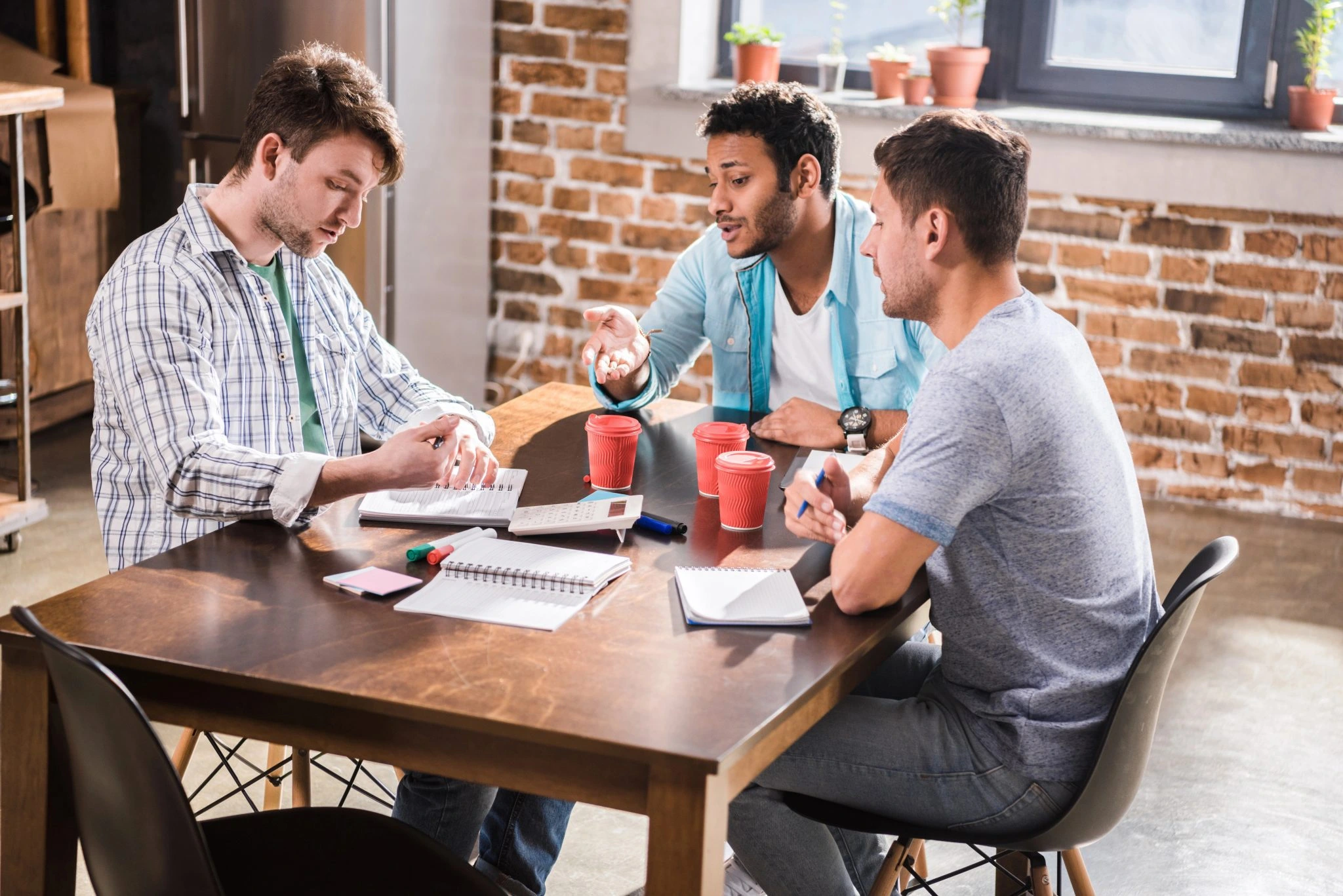 Three men seated at a table, collaborating over a laptop in a casual setting for ai readiness in marketing