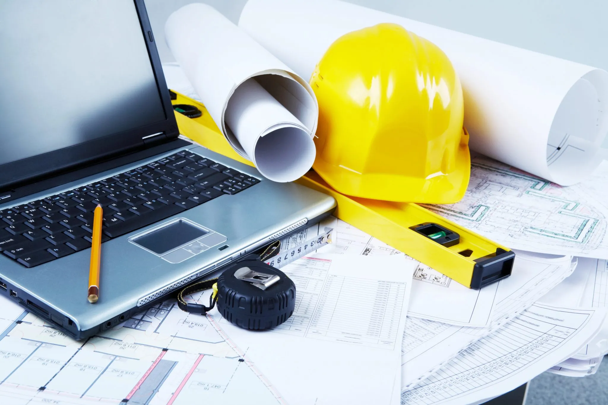 A laptop, construction plans, and a hard hat are arranged on a desk, indicating a work environment focused on building projects for marketing roi metrics for engineering b2b
