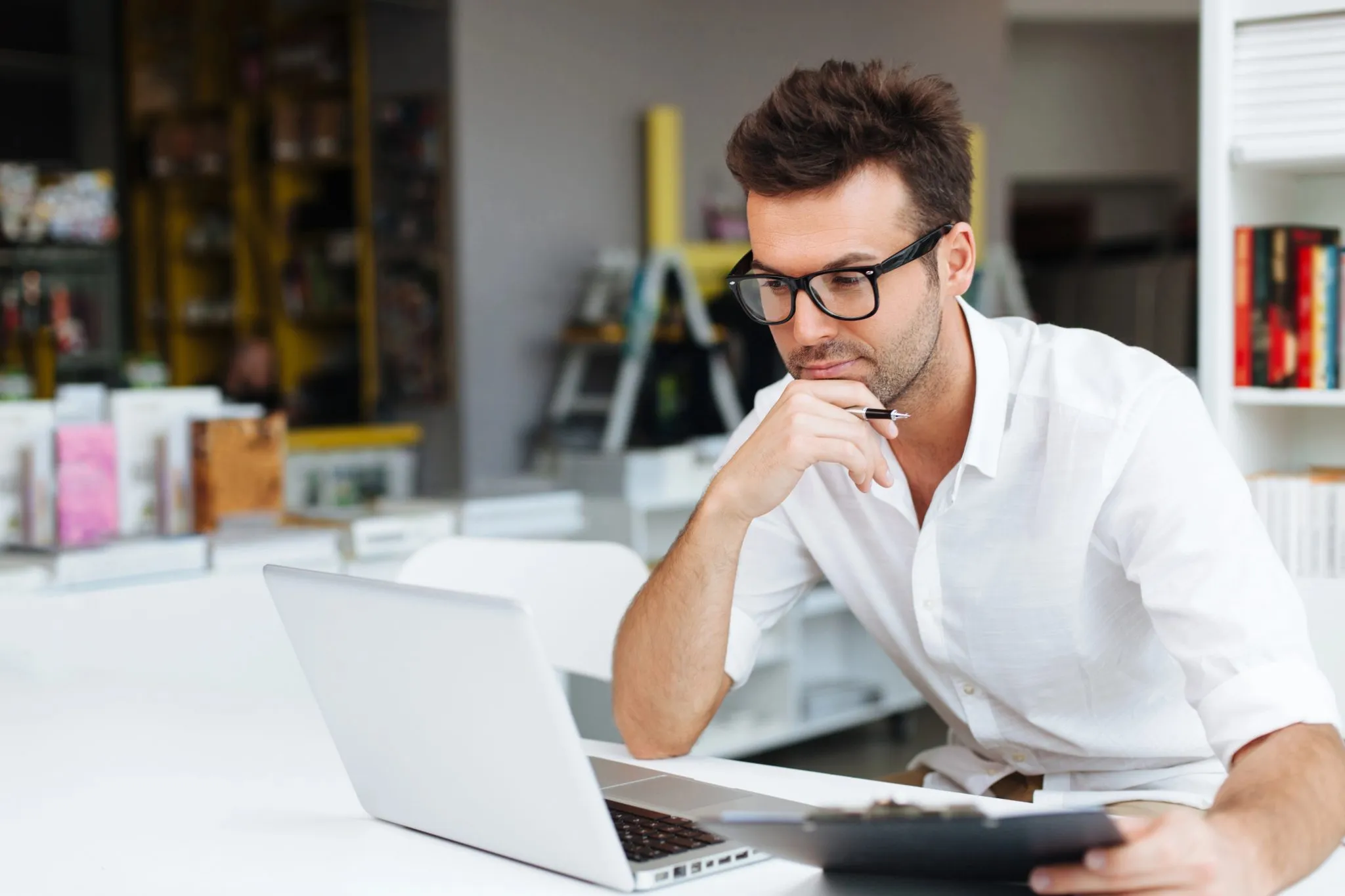 A man wearing glasses is seated at a desk, working on a laptop for b2b performance marketing strategies